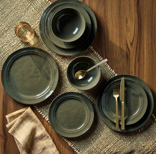 A array mounting with dark-toned ceramic dinnerware, golden cutlery, a glass, and a napkin connected a woven mat