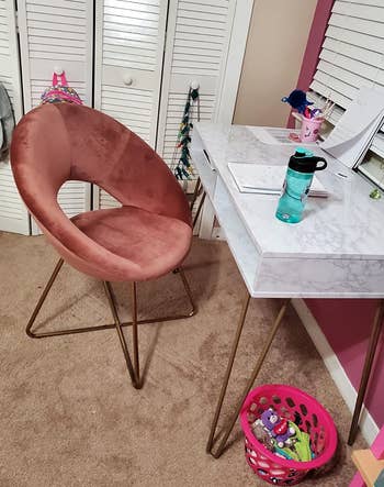 a reviewer photo of the chair in pink in front of a desk 