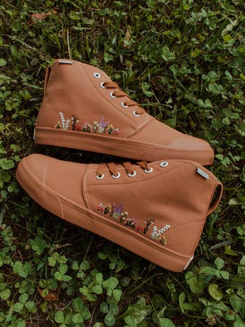 a pair of tan canvas hightop sneaker with floral embroidery in the grass