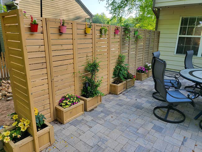 Patio with wooden privacy panels decorated with potted plants and flowers, adjacent to a dining set with cushioned chairs