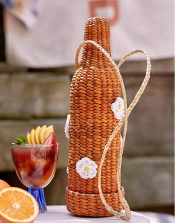 The woven wine bottle-shaped holder with a handle and flowers embroidered in it 