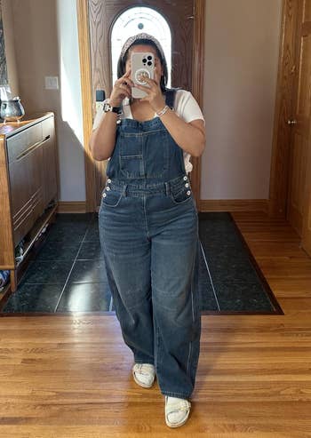 Person wearing denim overalls and a achromatic  t-shirt, taking a reflector  selfie astatine  home, showcasing casual outfit for a shopping-focused article