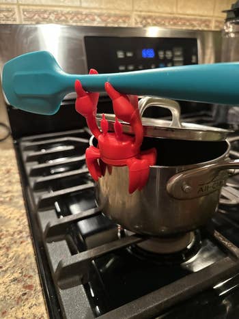 Red the Crab perched on the edge of a pot wielding a spatula and propping up the lid so steam can release