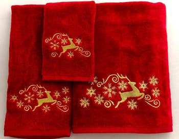 Three red towels adorned with gold reindeer and snowflake embroidery, suitable for holiday shopping