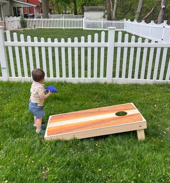 Child playing with a cornhole acceptable   successful  a backyard with a achromatic  picket fence