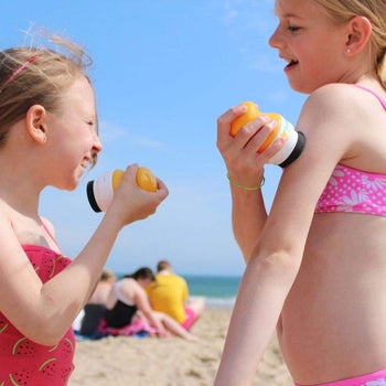 two children using the sunscreen applicator at the beach