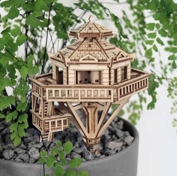 a wooden model house on a stake that's stuck in a houseplant 