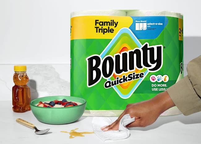 Person uses Bounty insubstantial towel to cleanable spilled liquid adjacent a vessel of effect and chromatic bottle. Package successful the background