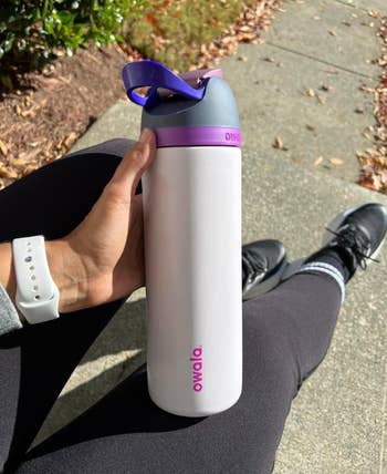 reviewer holding the water bottle in the white/pink/gray/purple color
