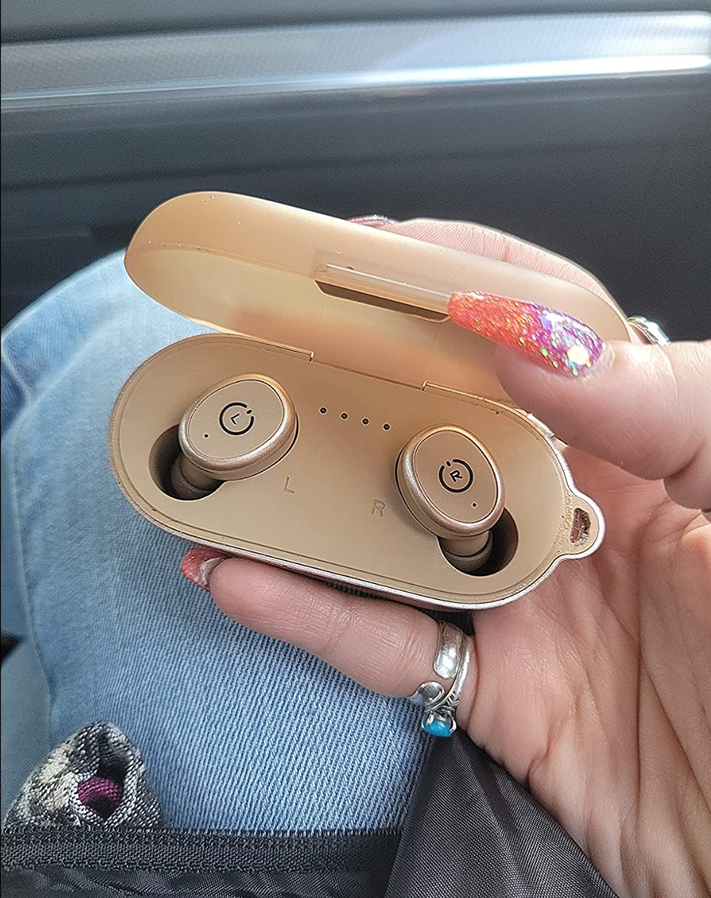 Reviewer holding pale pink earbud charging case with matching earbuds in them 