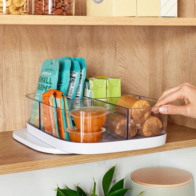 Rotating pantry organizer on a shelf, holding snacks and drinks, while a hand reaches for items