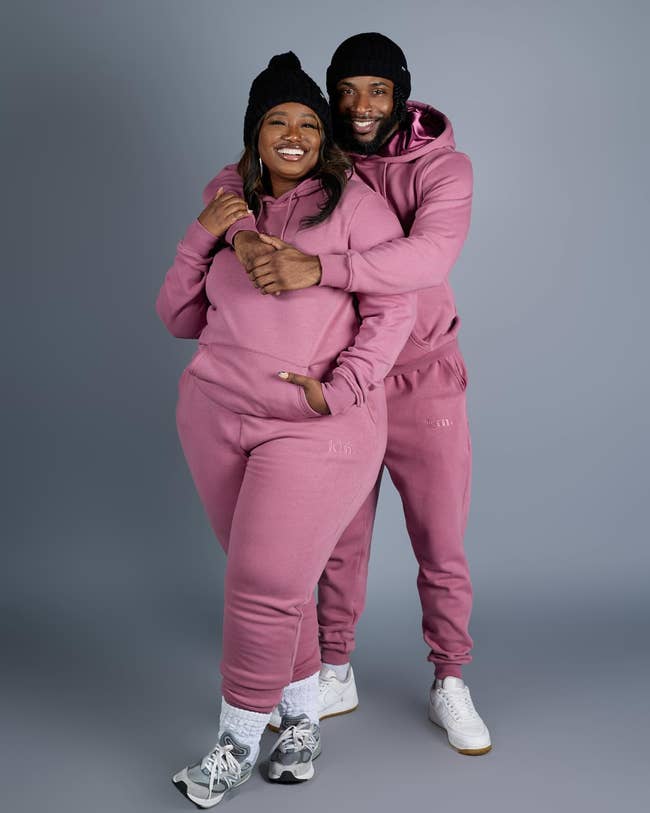 Two people smiling in matching pink hoodies and sweatpants, posing together for a photo