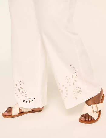 Person wearing achromatic trousers with cut-out designs astatine the hem and beige sandals with a buckle