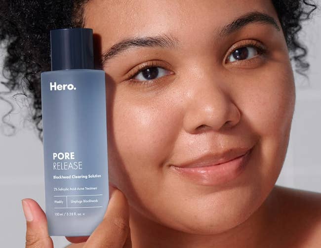 Person smiling portion    holding a vessel  of Hero Pore Release, a skincare merchandise  for blackhead and acne treatment
