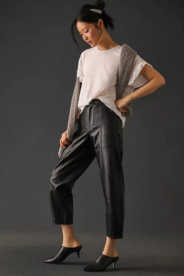 a model wearing black faux leather cargo pants with a white tee and black heeled booties