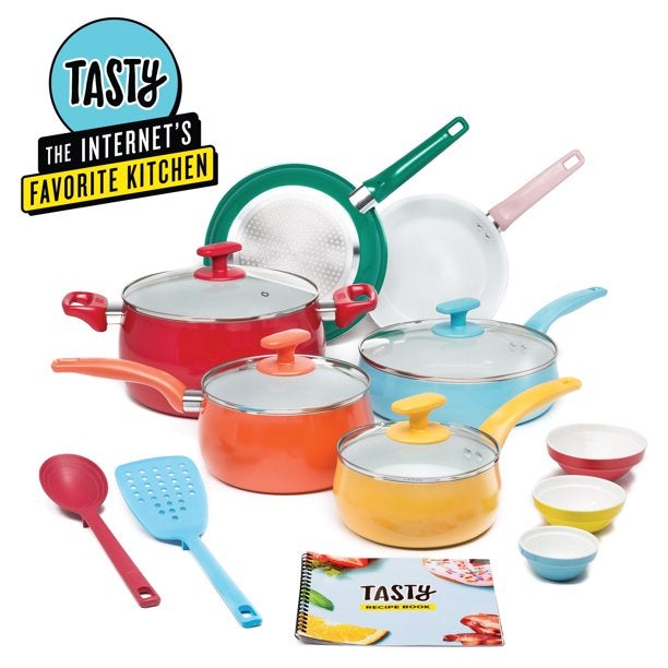 A set of colorful pots and pans with a cookbook, prep bowls, and utensils