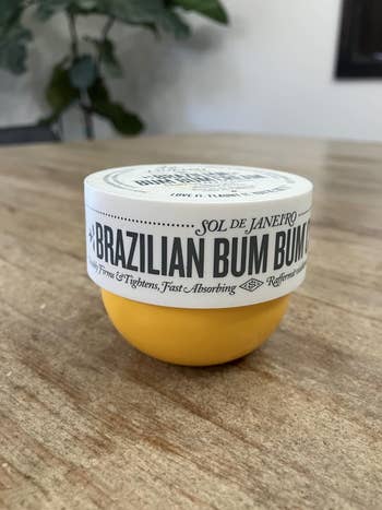 Jar of Sol de Janeiro Brazilian Bum Bum Cream connected  a woody  table, known for its fast-absorbing look   that firms and tightens skin
