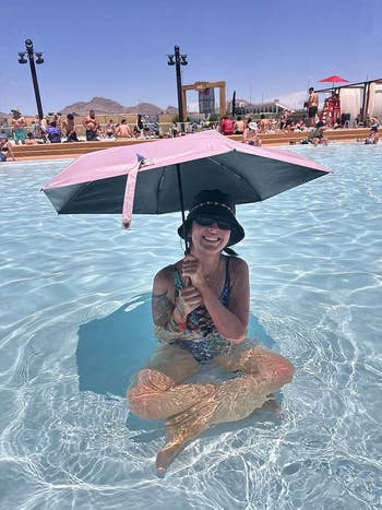 Person sitting in shallow pool, holding a sun umbrella