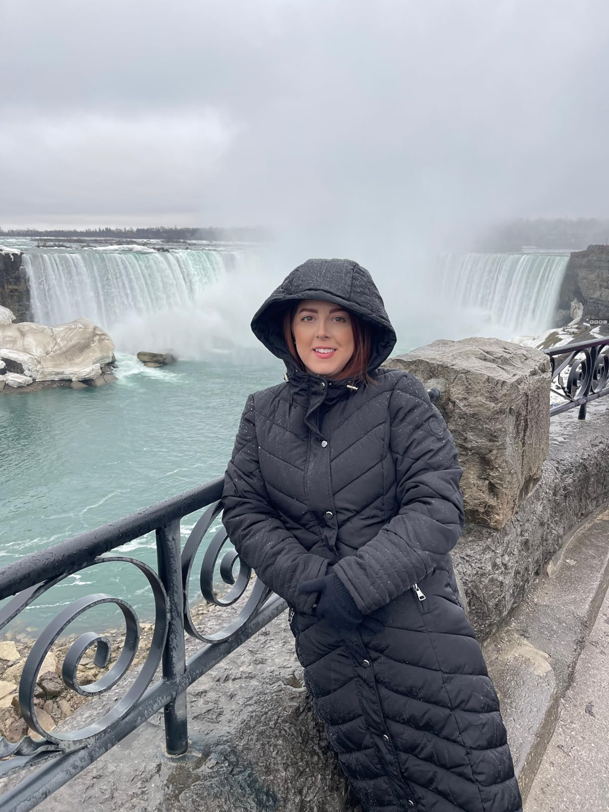 Person successful  a long, quilted overgarment  stands by a railing with ample  waterfalls successful  the inheritance  connected  a cloudy day