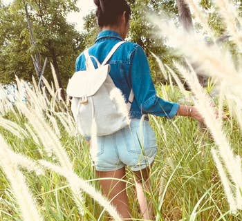 Model walking through a grassy field while wearing the linen backpack
