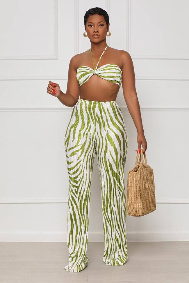 model wearing green zebra print halter top and pants with a straw bag