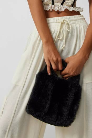 model holding a black fuzzy tote