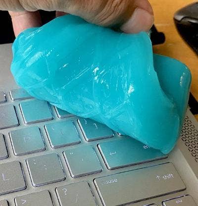 reviewer smushing the blue cleaning putty on a laptop keyboard