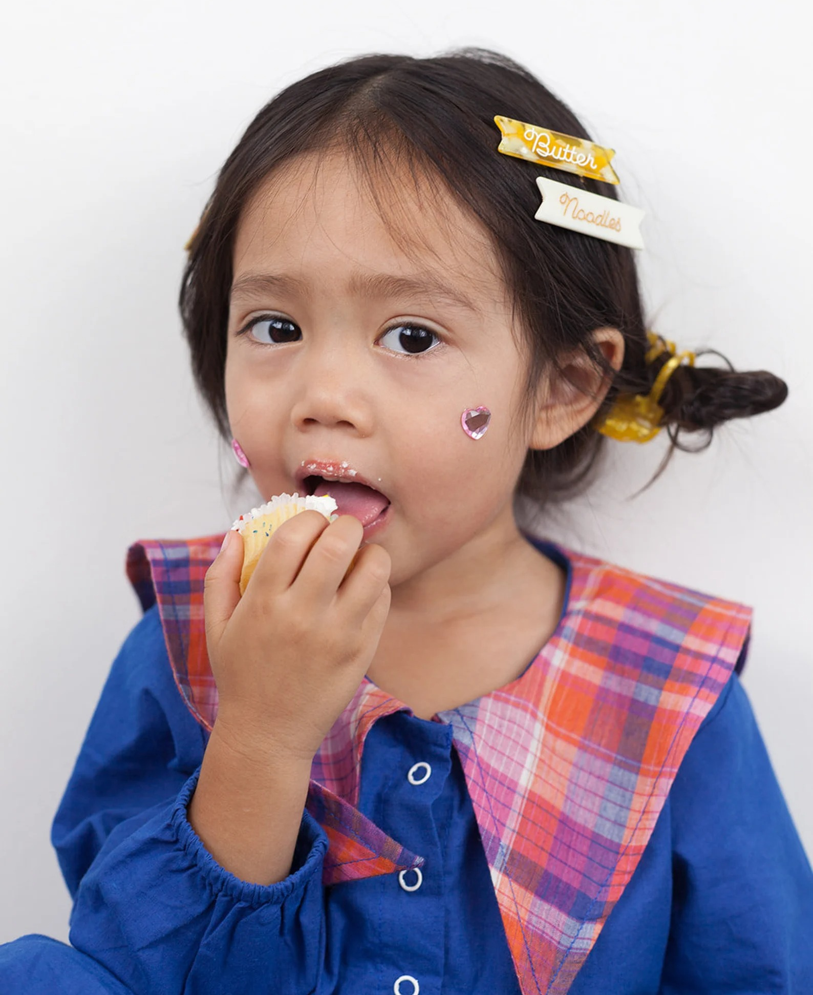 A child model with two clips in their hair: a yellow and white one that says butter and a white one that says noodles