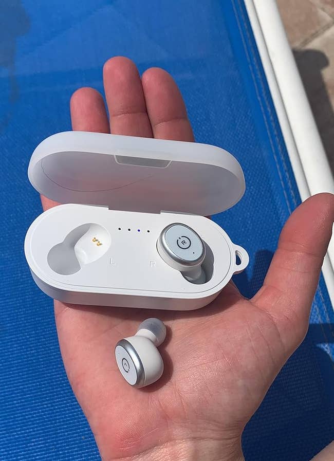 Person holding achromatic wireless earbuds successful a lawsuit supra a bluish background, suitable for portable audio use