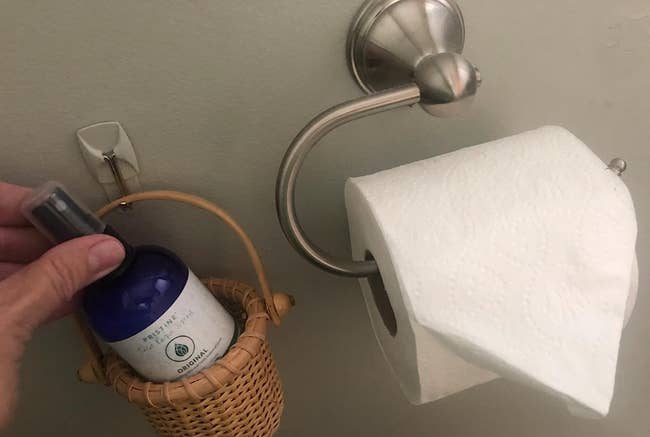 reviewer image of spray in basket beside toilet paper 