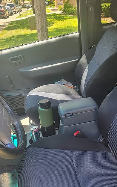 Inside of a reviewer's car showing a green water bottle in the cup holder adapter