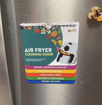 Air Fryer Cooking Guide hanging on a refrigerator, featuring categories for baking, poultry, meat, vegetables, and frozen foods