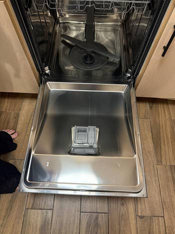 Open dishwasher with stainless alloy  interior and disposable   utensil racks, showing an bare  compartment acceptable   for loading dishes