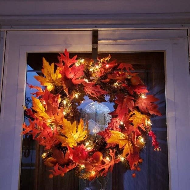 A fall-themed wreath with lights and autumn leaves hangs connected  a solid  door, creating a cozy, seasonal entrance