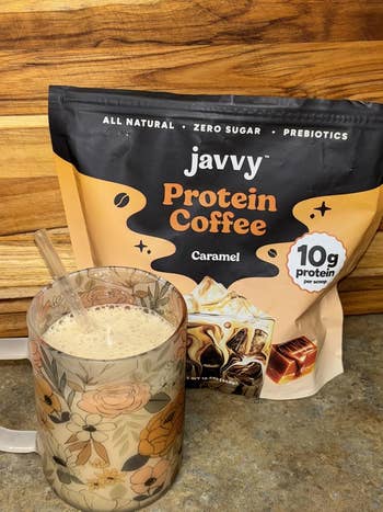Javvy Protein Coffee Caramel spirit bundle adjacent to a floral mug filled with a freshly made macromolecule java drink
