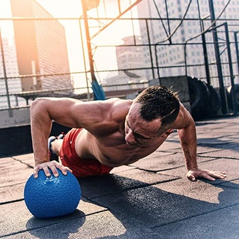 model completing push up and plank movements while pressing down on blue slam ball
