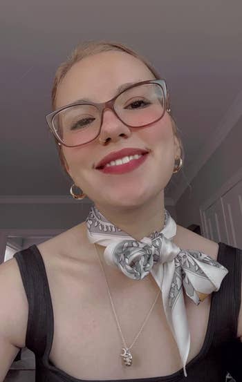 The reviewer smiling with glasses, scarf tied around neck, and a pendant necklace