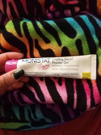 Hand holding a conduit of Monistat Care Chafing Relief Powder Gel against a colorful cloth background
