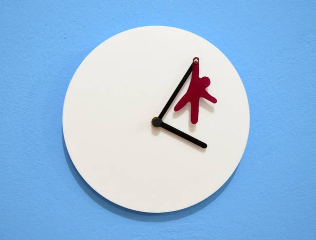 a white clock with a fuchsia cutout hanging from a clock hand 