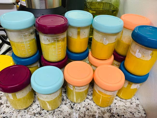 Glass jars filled with yellowish  babe  food, immoderate   capped with teal, purple, oregon  orangish  lids, connected  a speckled countertop
