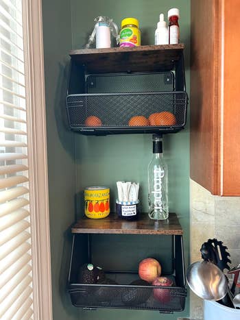 Wall-mounted room  support  with baskets holding oranges, avocado, apple, canned tomatoes, and assorted  spices. Utensils remainder  connected  the counter