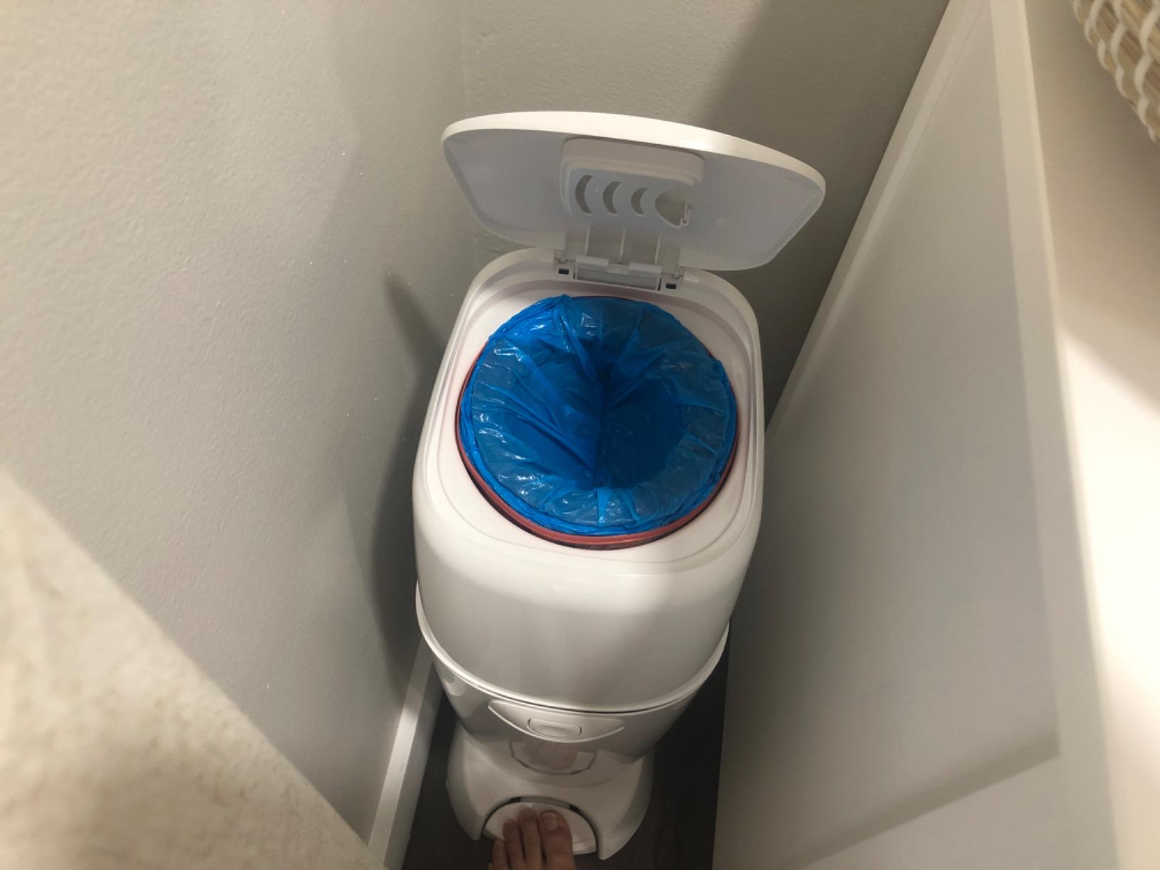 Diaper pail with lid unfastened  revealing a bluish  liner inside, placed successful  a constrictive  bath  corner