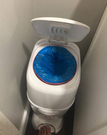 Diaper pail with lid unfastened revealing a bluish liner inside, placed successful a constrictive bath corner