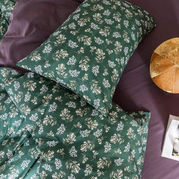 a dark green floral printed pillow and blanket on top of dark purple bedding