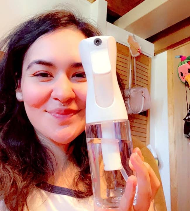 reviewer smiling and holding the white spray bottle