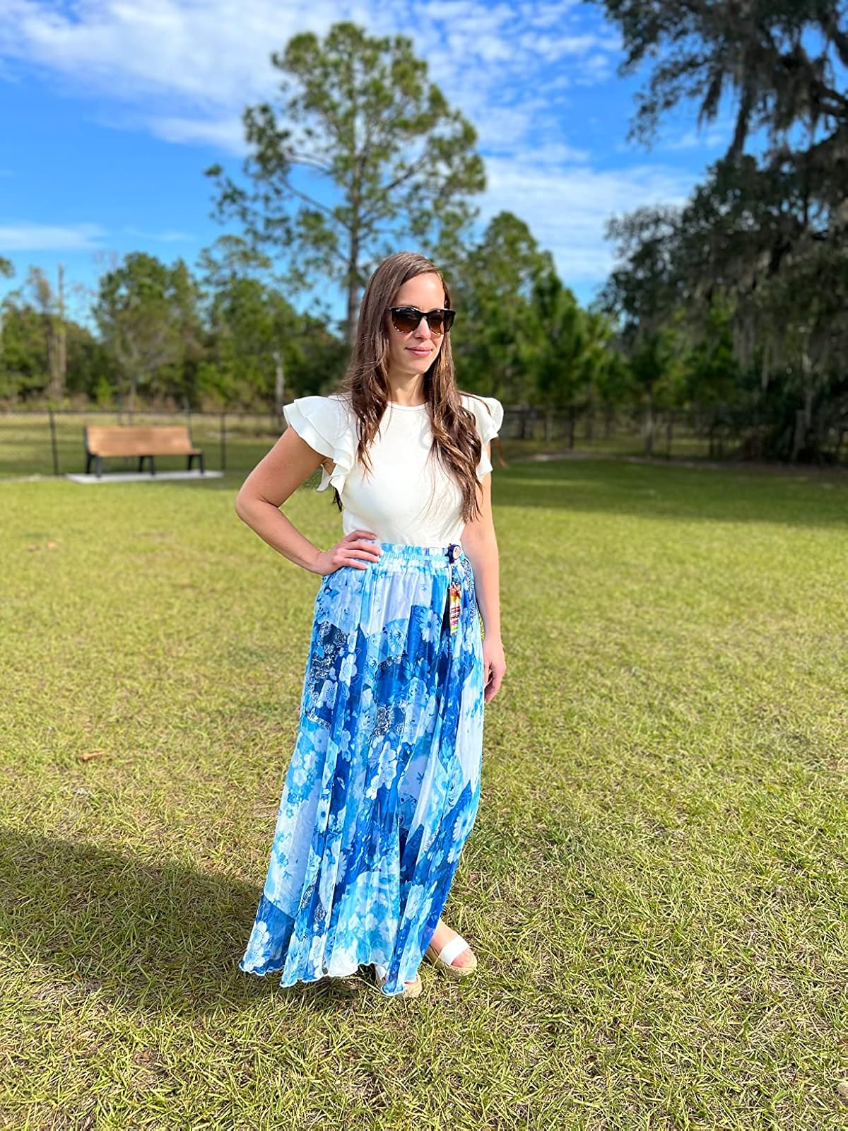 A Reviewer outdoors wearing a white ruffle-sleeve top, a flowing patterned skirt, and sunglasses