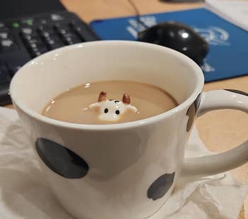 Cow-themed mug with a ceramic cattle fig peeking retired from the java inside, placed connected a napkin adjacent a machine keyboard and mouse
