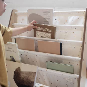 Child selecting a book from a fabric bookshelf filled with various children's books in a cozy, organized setting