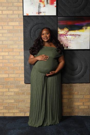 Person successful  an off-the-shoulder, pleated formal  with hands connected  their belly, lasting  against a textured partition  with abstract art. Suitable for maternity shopping