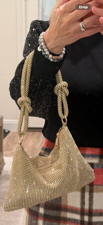 Person holding a stylish beaded handbag with knot details, wearing a glittery long-sleeve top